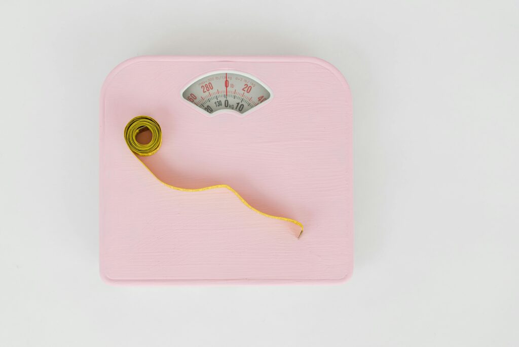 Pink scale with a rolled-up tape measure placed on top, symbolizing weight and measurements.