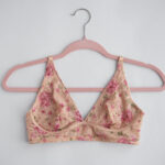 A pink floral bra hanging on a pink hanger with a white background.