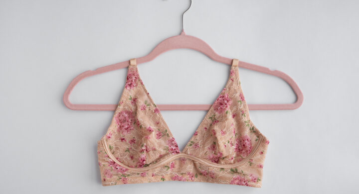 A pink floral bra hanging on a pink hanger with a white background.