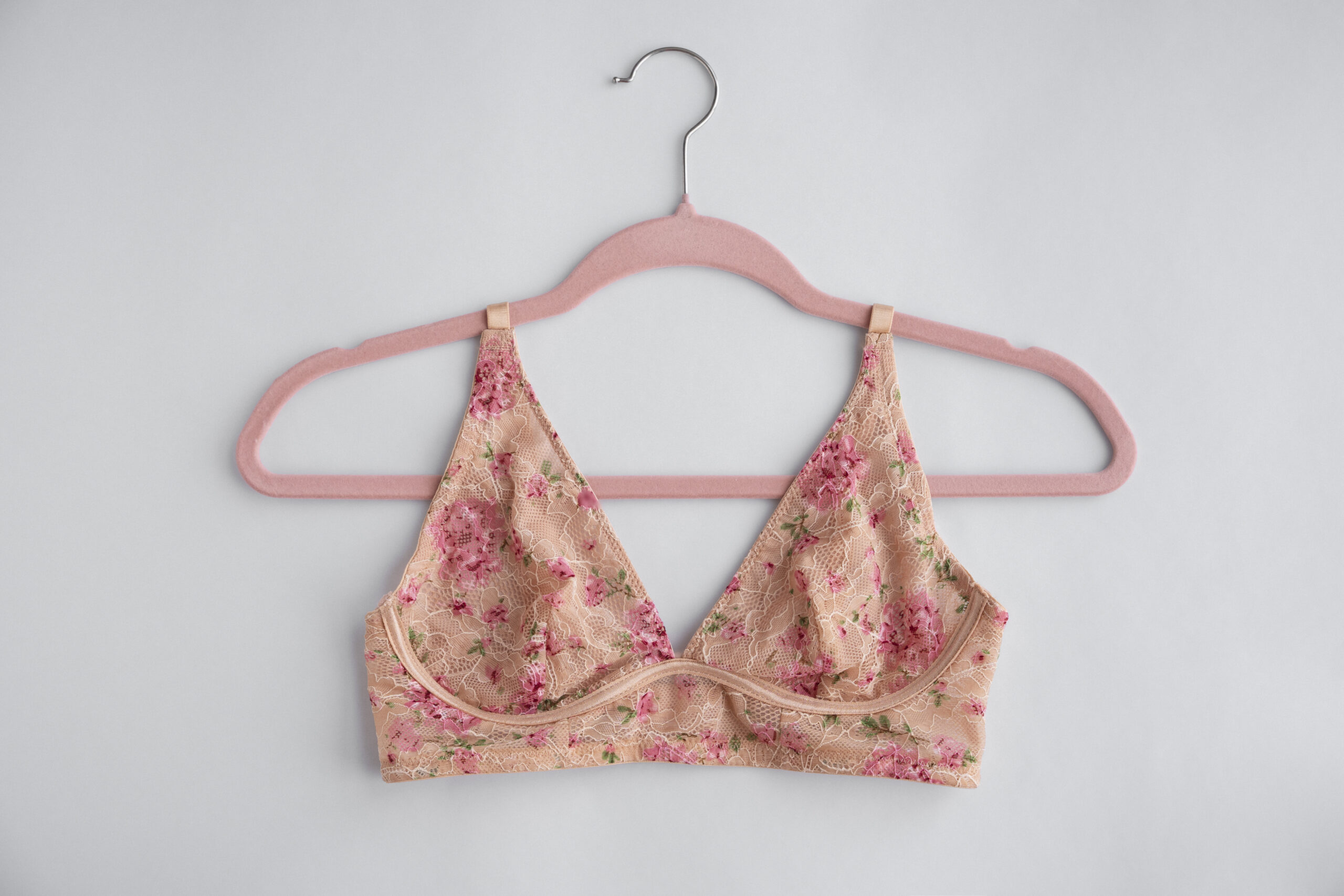 A pink floral bra hanging on a pink hanger with a white background.