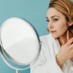 A woman looks at her neck and jawline in a mirror.