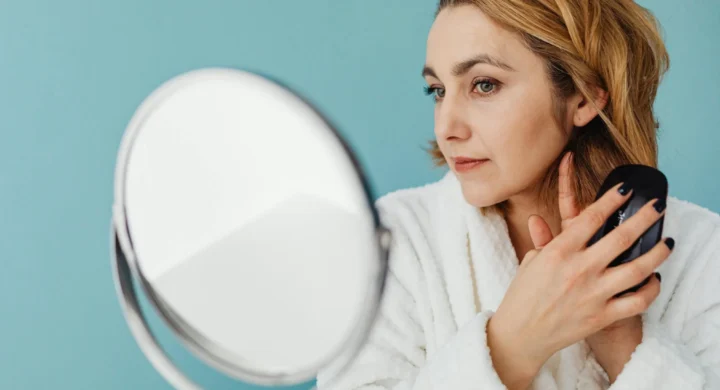 A woman looks at her neck and jawline in a mirror.