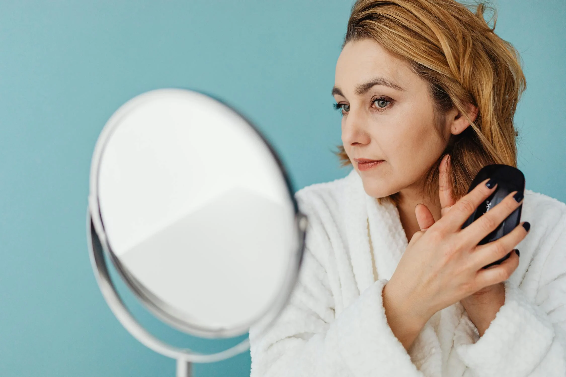 A woman looks at her neck and jawline in a mirror.