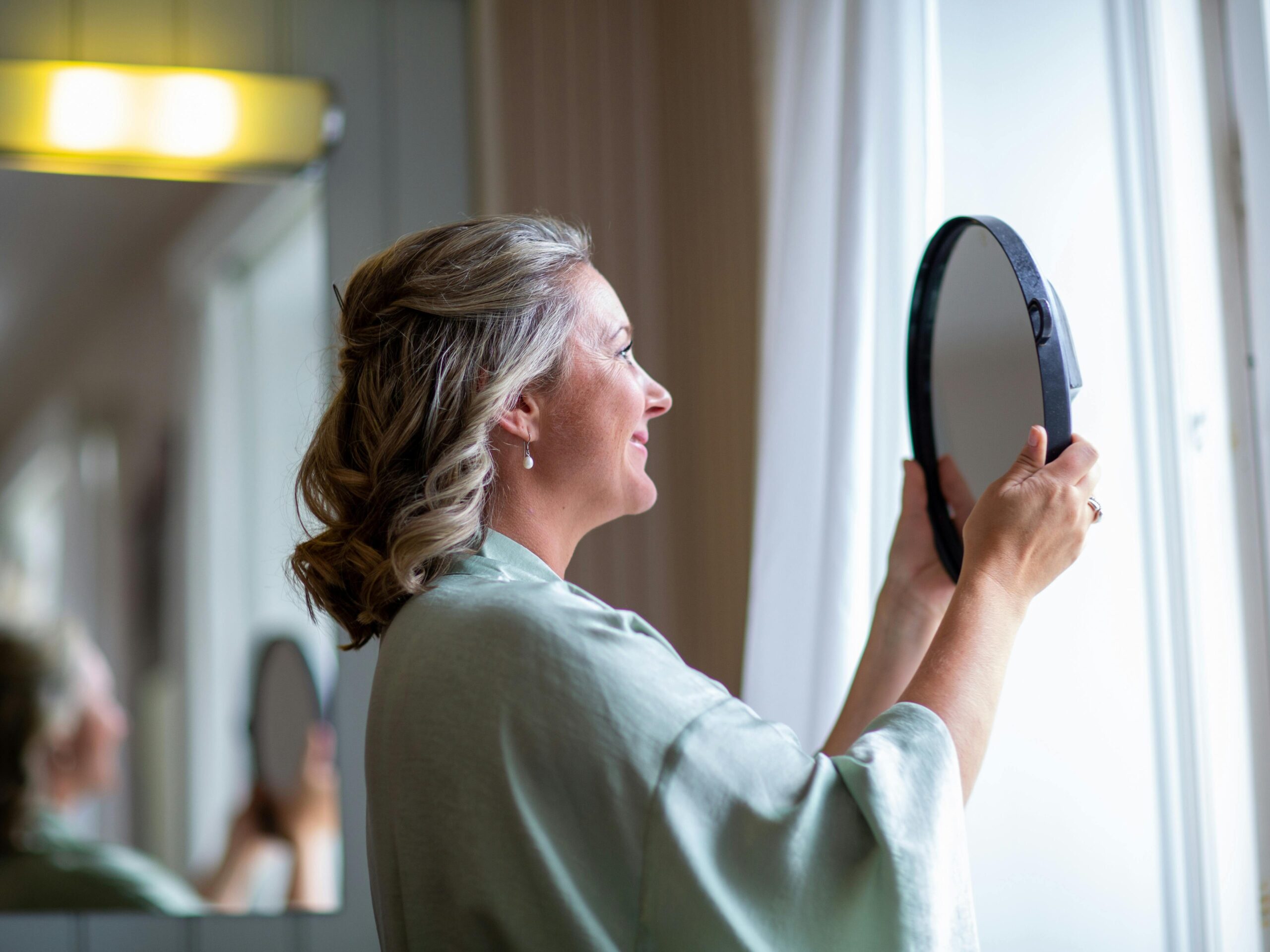 Older woman smiling while looking at her reflection in a mirror from a side profile view.
